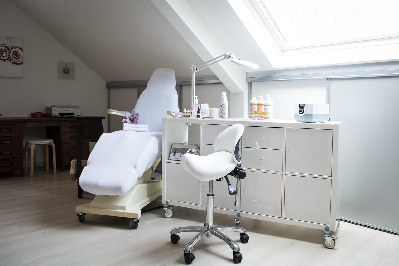 A bright beauty room with a white treatment couch and stool