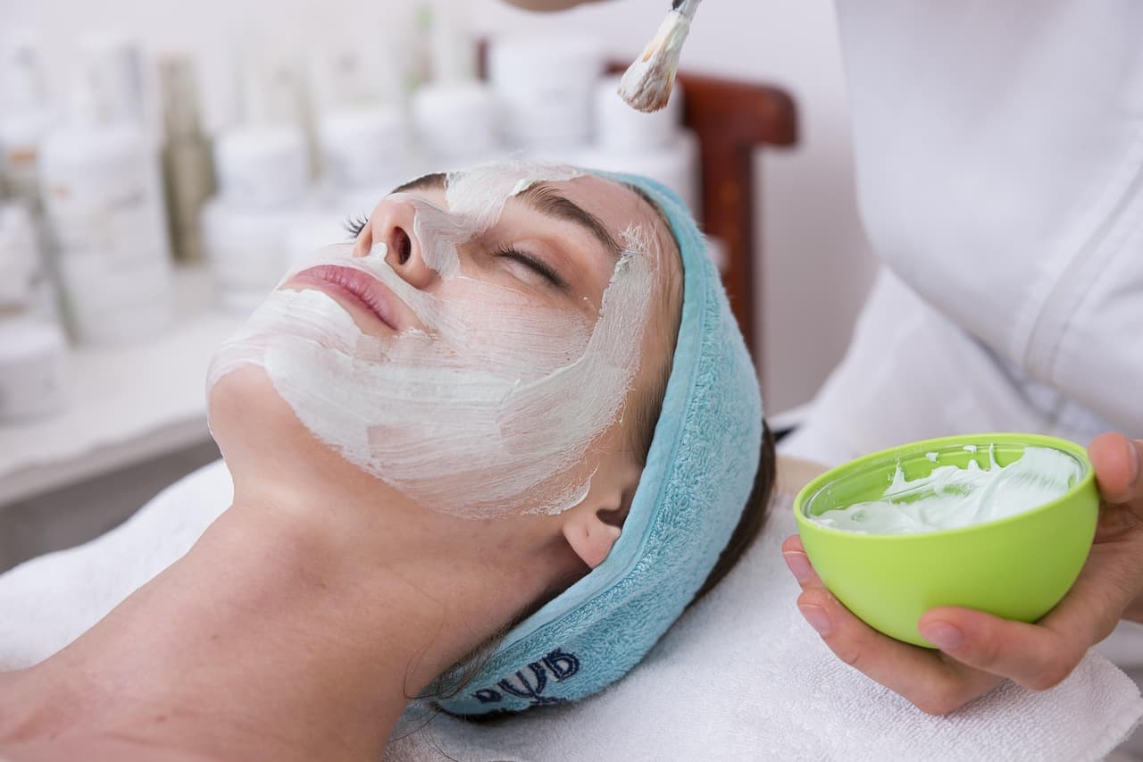 A facial mask being brushed on as a client lies back on a towel