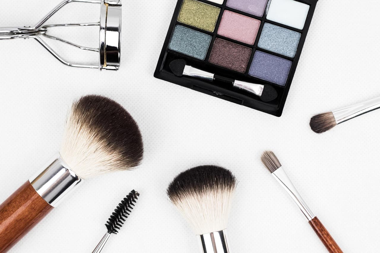Make-up brushes, an eyeshadow palette and a lash curler on white