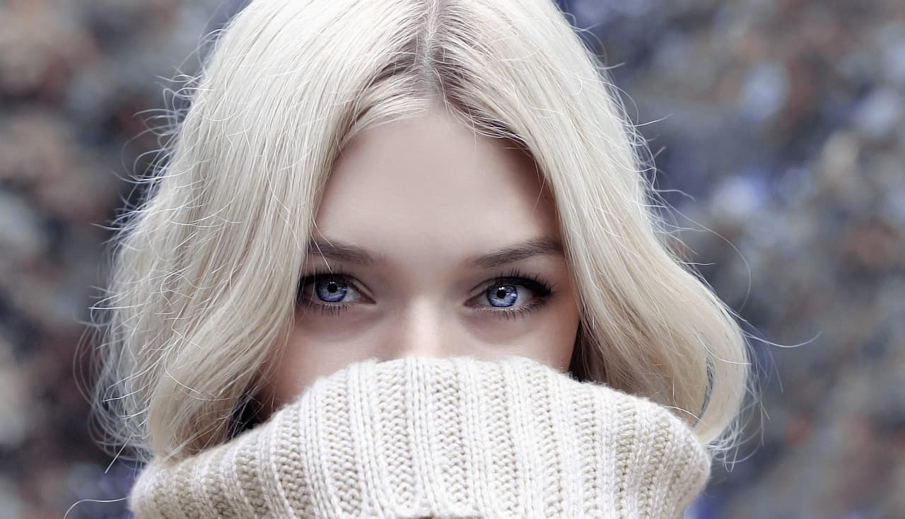 A woman with soft, even brows, a knitted sweater pulled up to her nose